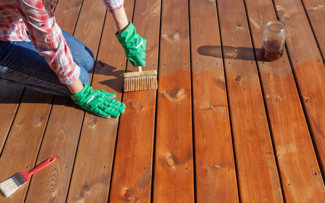 A woman meticulously applying a maintenance product to her deck, showcasing the importance of regular upkeep to keep the deck looking fresh and well-maintained year-round